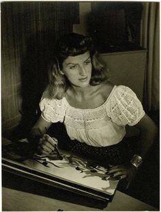 a woman sitting at a table writing on a piece of paper in front of a lit candle