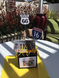 a table topped with two street signs next to a yellow cloth covered chair and potted plant