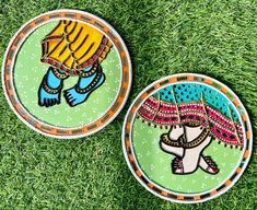 two decorative plates sitting on top of green grass covered in dirt and paint, one with an image of a woman holding a parasol