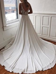 a woman standing in front of a window wearing a white wedding dress with spaghetti straps