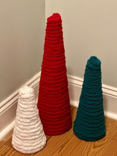 three knitted christmas trees sitting on the floor in front of a wall with white trim