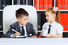 two young children sitting at a desk in front of books and holding coffee mugs