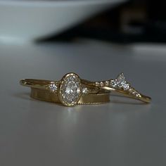 two gold wedding rings with diamonds on them sitting on a counter top next to a bowl