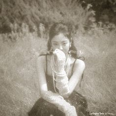 a woman sitting in the grass with her hands on her face and holding something up to her mouth