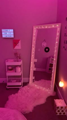 a pink room with a mirror and lights on the wall, next to a bed