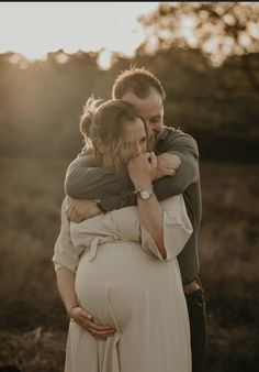 a pregnant woman hugging her husband while the sun is setting