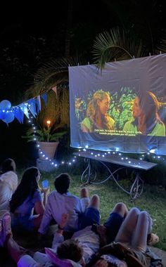 people sitting in the grass watching a movie on an outdoor projector screen at night