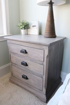 a bedroom with a dresser and lamp in it's corner, next to a window