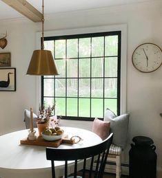 a dining room table and chairs with a clock on the wall behind it in front of a window