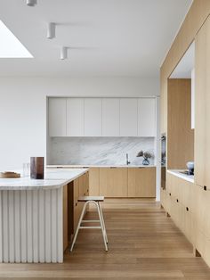 an empty kitchen with wooden floors and white counter tops, along with stools in front of the island