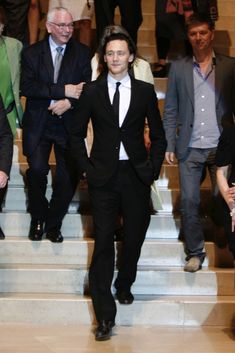 a man in a suit and tie walking down some steps with other people behind him