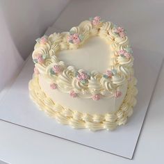 a heart - shaped cake with white frosting and pink flowers on the top is displayed