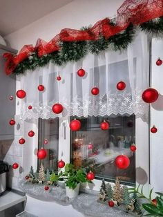 a window with christmas decorations hanging from it's side and red balls on the windowsill