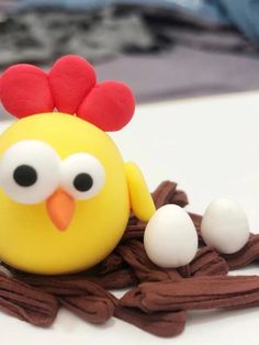 a yellow toy chicken sitting on top of a pile of brown string with eggs in it's beak