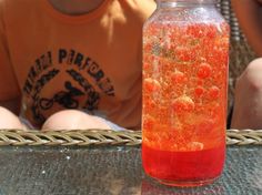 a jar filled with red liquid sitting on top of a table next to a person