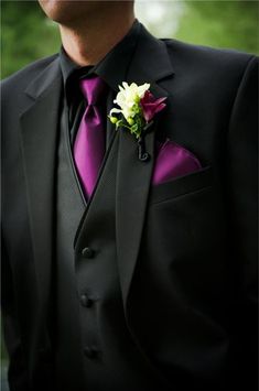 a man in a black suit with a purple tie and flower boutonniere