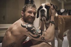 a man sitting on the floor with his dog in his lap and tattoos on his arm