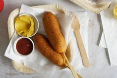 two hotdogs with mustard and ketchup are on a plate next to other food