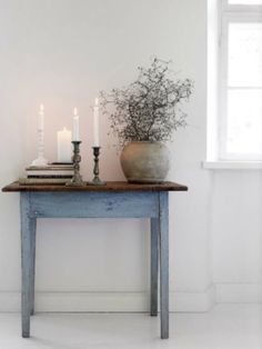 an old table with candles and books on it, next to a potted plant