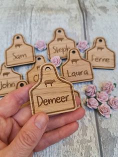 hand holding wooden name tags with flowers around them on a white wood background, which says demer