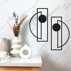 a vase with some flowers on a table next to a wall mounted art piece in the shape of circles and rectangles