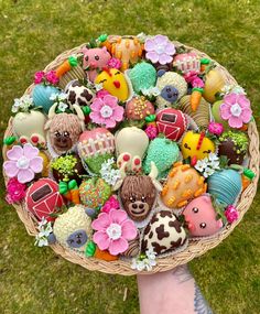 a person holding a basket filled with lots of different types of decorated cookies on top of green grass