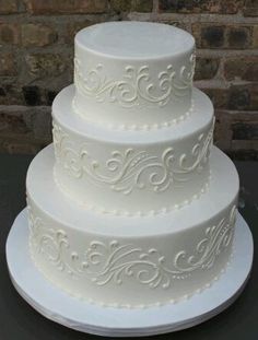 a three tiered white wedding cake sitting on top of a black countertop next to a brick wall