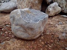 a large rock sitting on top of a dirt ground next to rocks and gravel covered ground