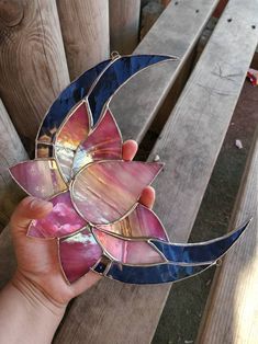 a hand holding a stained glass sun catcher on top of a wooden bench next to a fence