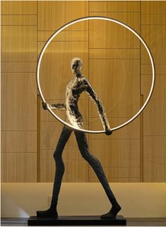 a statue holding a large metal hoop in front of a wooden paneled wall and floor