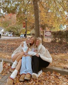 two women sitting on the ground with their arms around each other and holding coffee cups