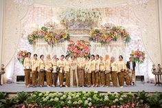 a group of men standing on top of a stage next to flowers and greenery