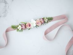 a pink ribbon with flowers and leaves is on a marble surface next to a white wall