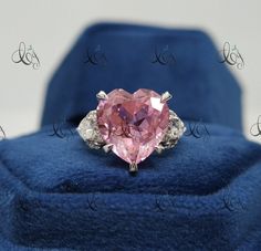 a pink heart shaped diamond ring sitting on top of a blue velvet cushioned box