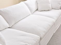 a white couch with four pillows on top of it in a room that has carpeted flooring