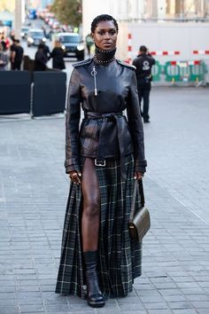 a woman standing on the street wearing a long skirt and black leather jacket with high slits