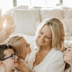 a woman and two children are sitting on a couch together, with the child's mother kissing her cheek