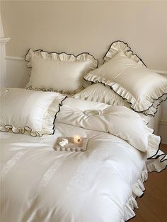 a bed with white sheets and pillows on top of it next to a lit candle