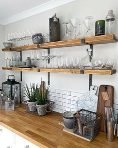 the shelves are filled with wine glasses and other kitchen items on wooden countertops in front of white brick walls