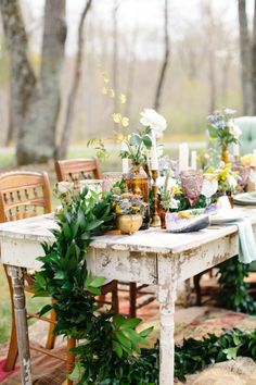 the table is set with flowers and greenery for an outdoor dinner party in the woods