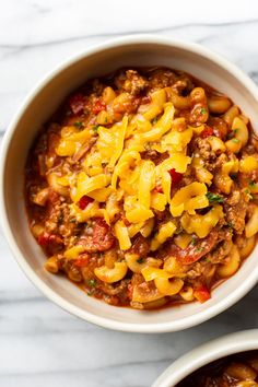 two white bowls filled with chili macaroni and cheese on top of a marble table