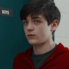 a boy in a red hoodie standing next to a green wall