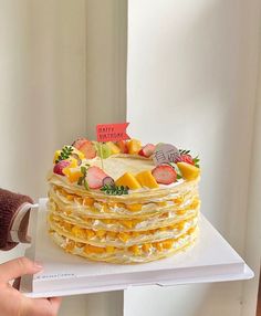 a person holding up a cake made out of pancakes with fruit toppings on top