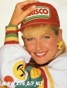 a woman with blonde hair wearing a red hat and smiling at the camera while holding her hand up to her head