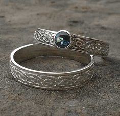 two silver rings with a blue stone in the middle on top of cement ground next to each other