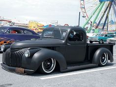 an old black truck parked in a parking lot next to a ferris wheel at a carnival