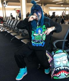 a woman with blue hair sitting on an airport bench next to a backpack and handbag