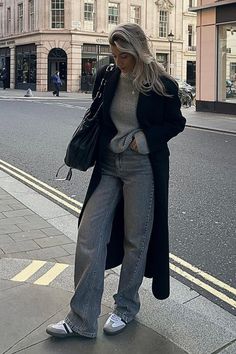 a woman is standing on the sidewalk with her hand in her pocket and looking down