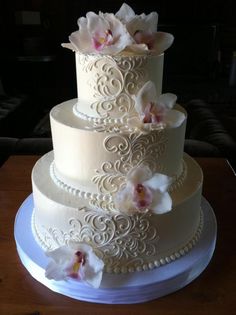 a three tiered wedding cake with white flowers on the top and bottom, sitting on a table