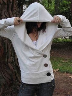 a woman standing in front of a tree with her hood up